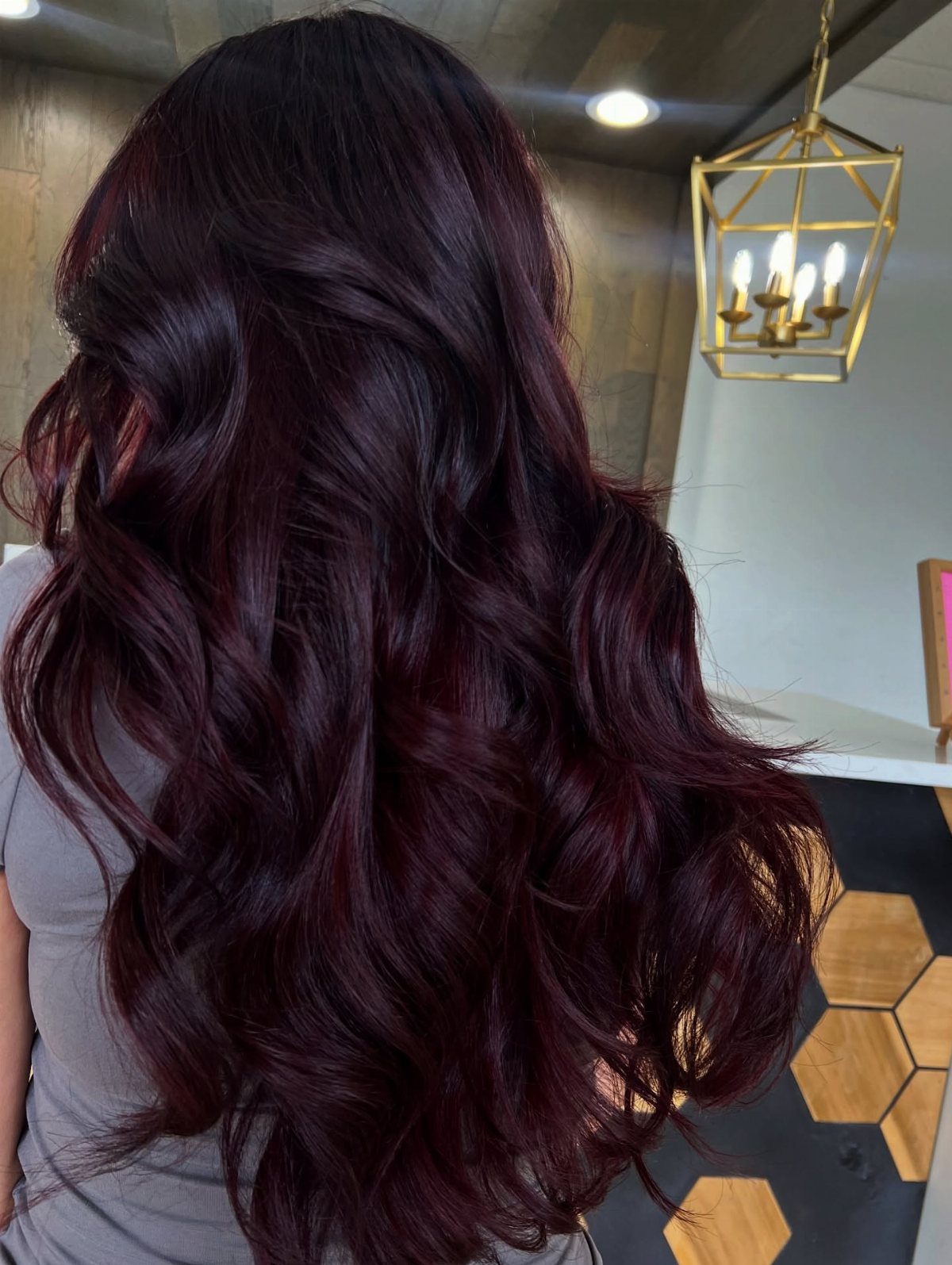 Long, wavy black cherry hair with burgundy highlights shown from behind in a salon