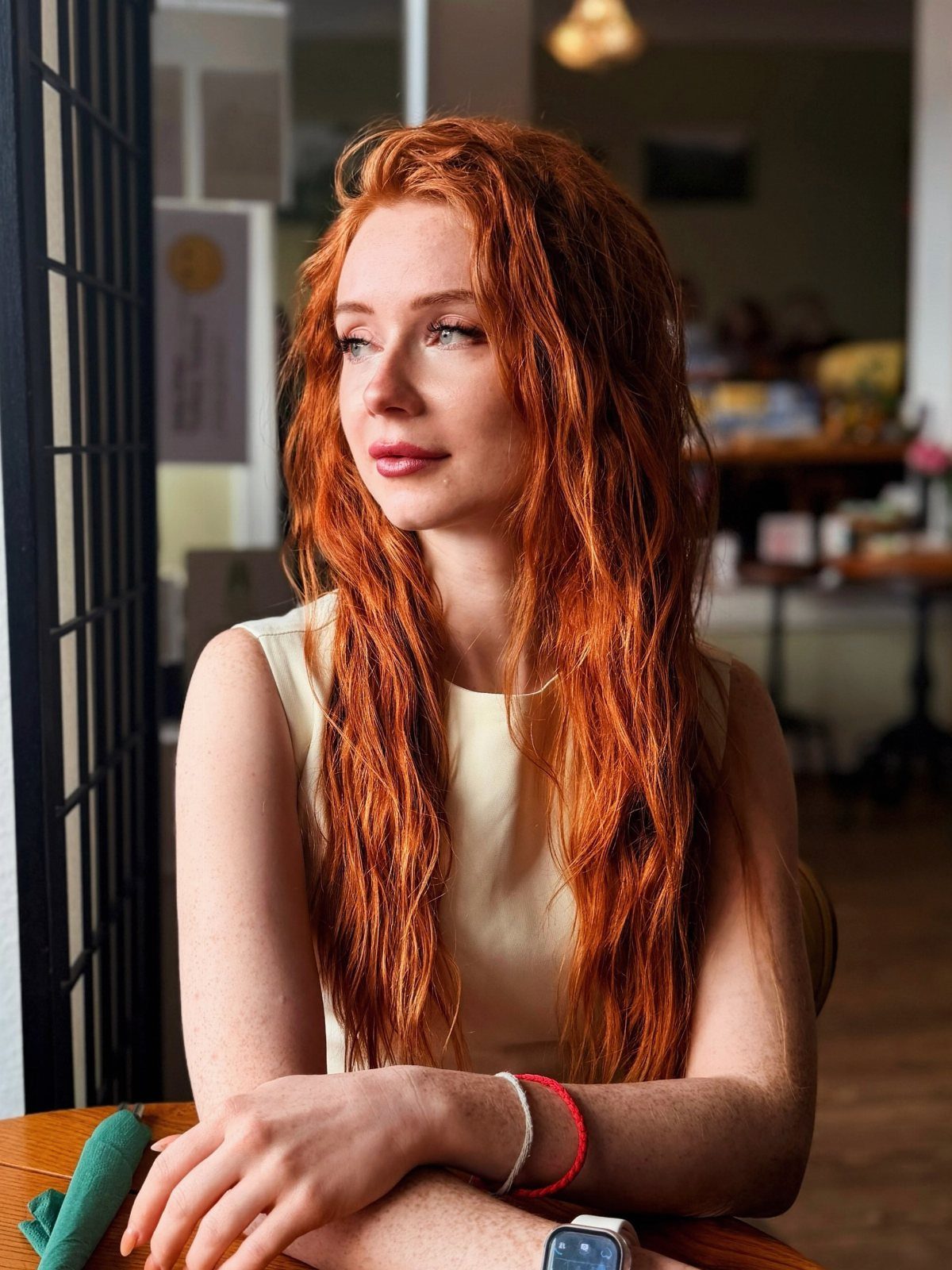 Woman with long, wavy bright copper-red hair sitting indoors