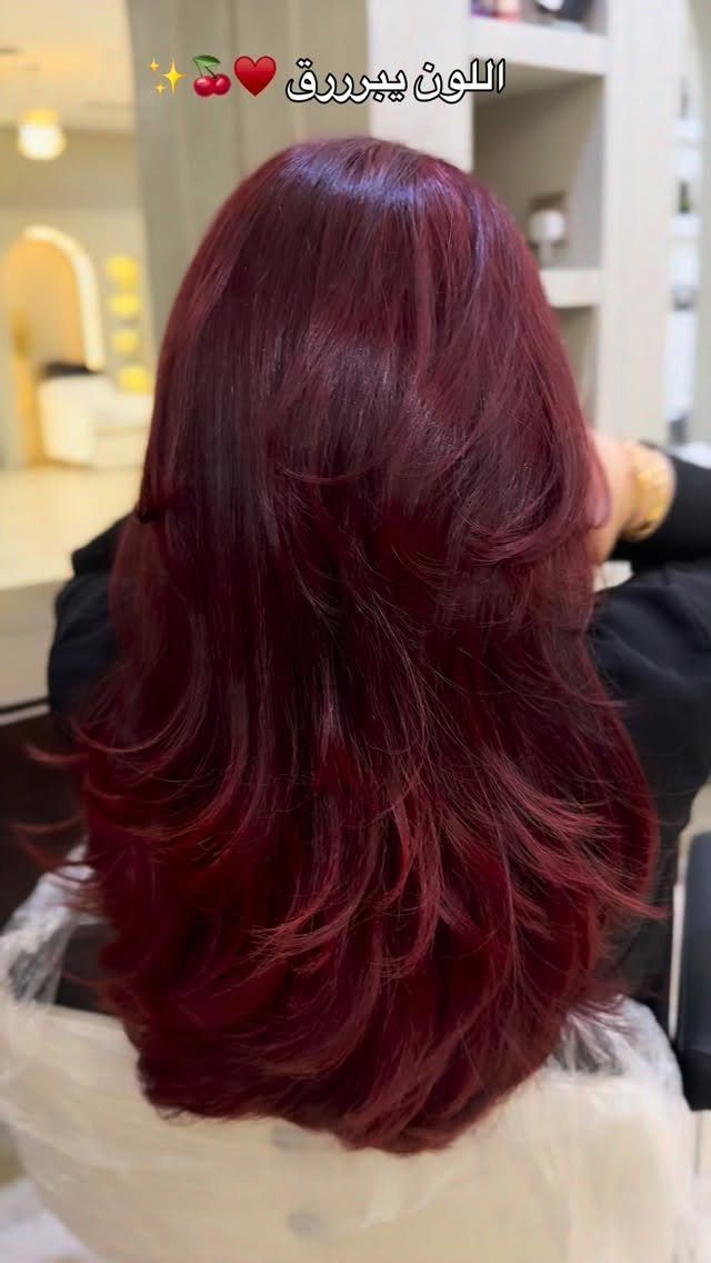 Long layered burgundy-red hair styled in glossy waves at a salon