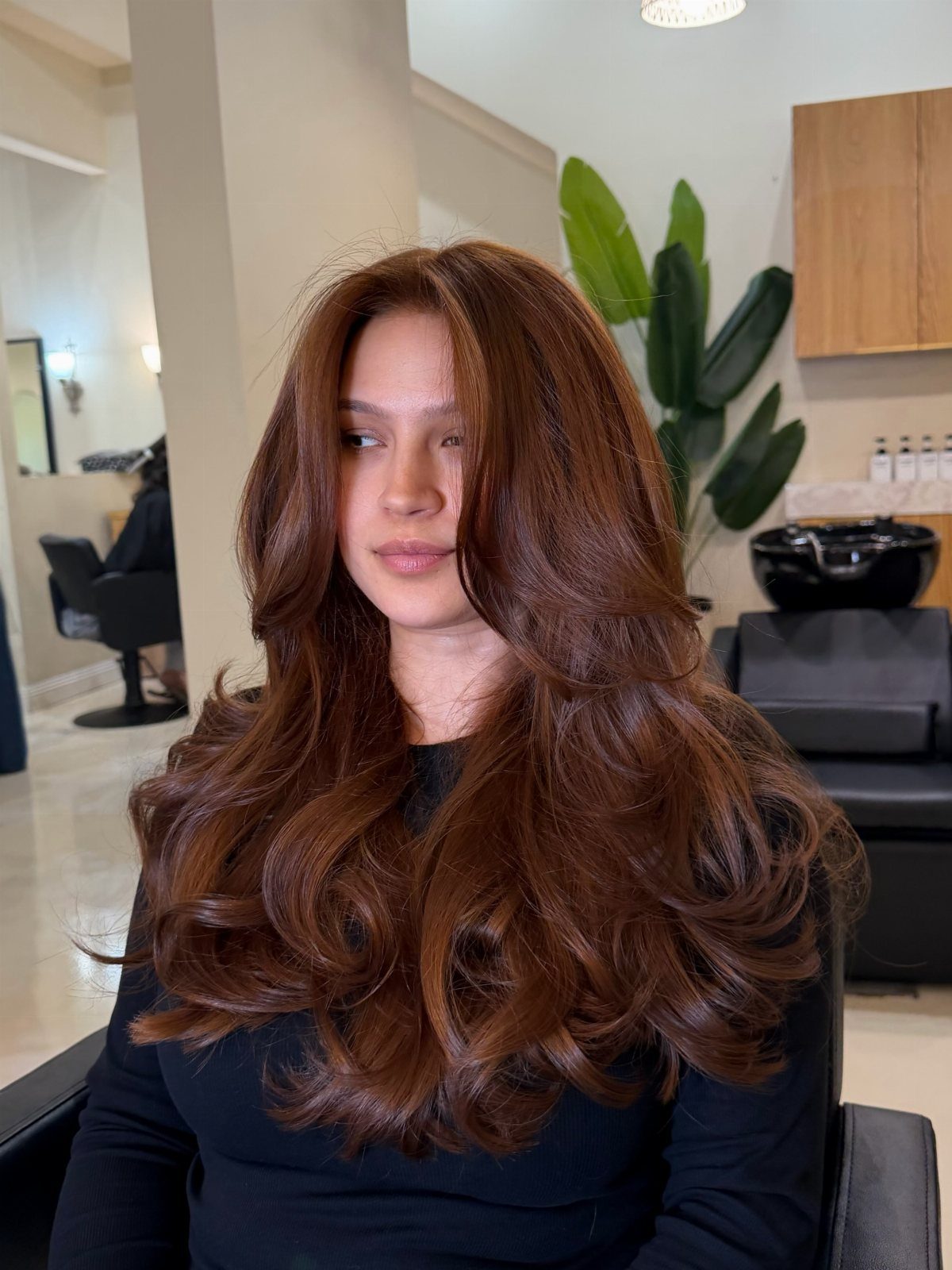 Woman displaying long, glossy copper-brown curls in a salon