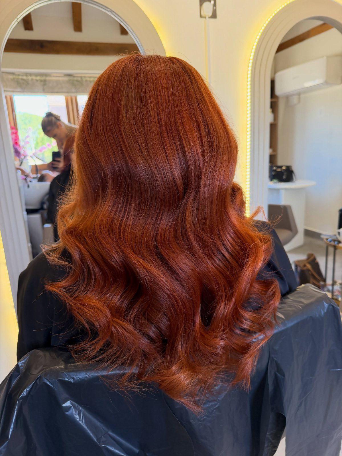 Glossy auburn-red curls fall down a salon client's back
