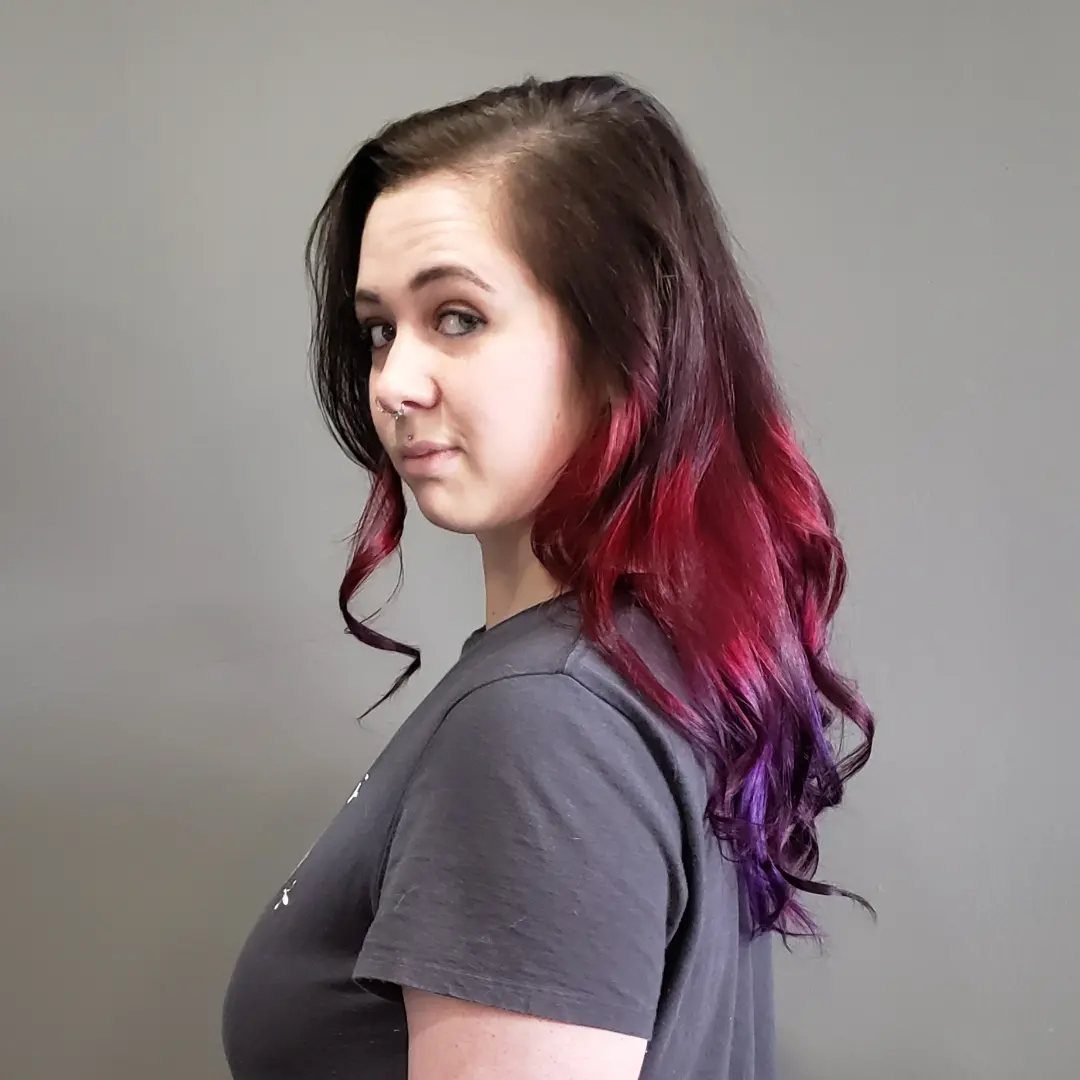 Woman showing wavy hair transitioning from dark roots through red to purple ends