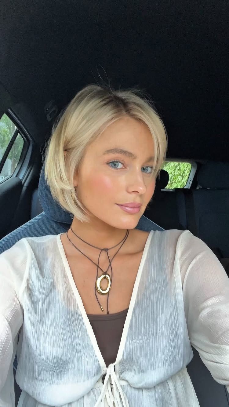 Woman posing in a car with a short blonde, softly layered bob