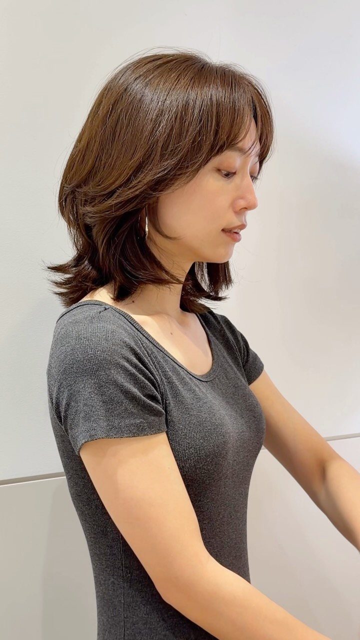 Woman with a layered brown lob, side-swept bangs, and feathered ends