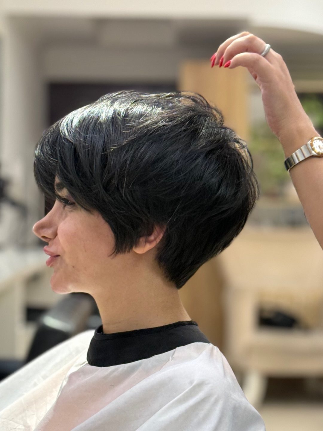 Short dark pixie with side-swept bangs shown in profile at a salon