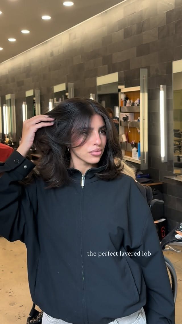 Woman showing dark shoulder-length layered hair with softly curved ends in a salon