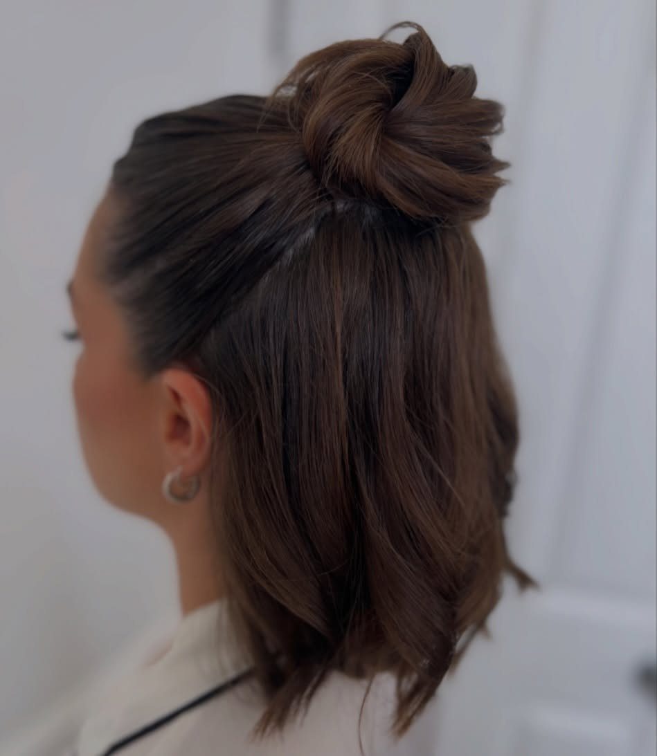 Dark brown shoulder-length hair styled half-up in a small crown bun