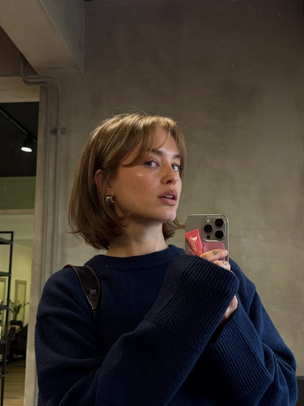 Woman with a layered brown bob and face-framing pieces takes a mirror selfie.