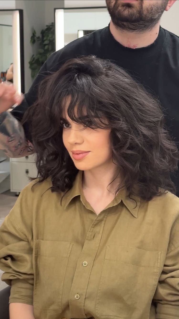 Shoulder-length dark layered hair with soft waves and curled ends in a salon
