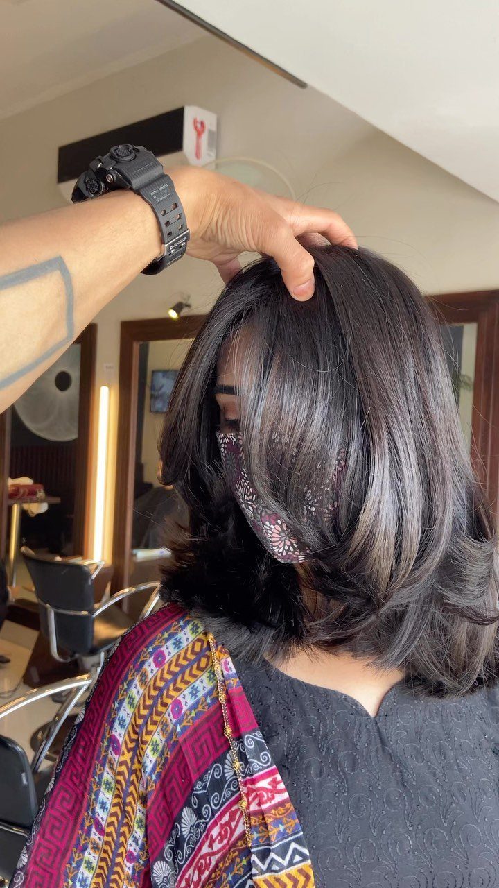 Glossy dark shoulder-length hair showing defined, curved layers in a salon