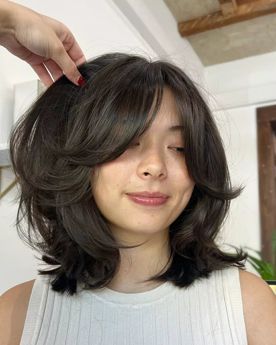 Dark shoulder-length hair with defined, flipped layers and curtain bangs